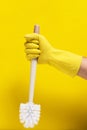 Hand yellow rubber glove holds toilet cleaning brush yellow background.