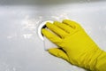 A hand in a yellow rubber glove with a melamine sponge rubs the wet dirty white bath or the sink near the drain hole Royalty Free Stock Photo