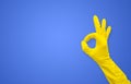 Hand in a yellow rubber glove shows the gesture & x22;okay& x22; on a blue background with copy space Royalty Free Stock Photo