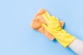 Hand in a yellow rubber glove washes the wall with an orange soft rag, cleaning and washing the walls, blue background copy space Royalty Free Stock Photo