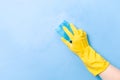 a hand in a yellow rubber glove washes a wall with a wet foamy blue sponge, foam blue background copy space Royalty Free Stock Photo