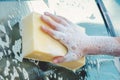 Hand with yellow sponge and soap are washing a car