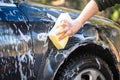 Hand with yellow sponge and soap are washing the car