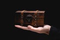 The hand of a young Caucasian woman holds a small wooden chest on a black background. Low key Royalty Free Stock Photo