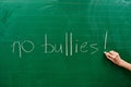 Hand of a young girl writing the words NO BULLIES on the green school board