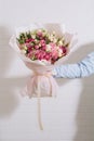 The hand of young man in a blue classic shirt holds a big bouquet of white pink roses and eustoma in pink packaging on the white Royalty Free Stock Photo