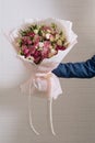 The hand of young man in a blue classic suit holds a big bouquet of white pink roses and eustoma in pink packaging on the white Royalty Free Stock Photo