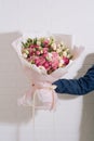 The hand of young man in a blue classic suit holds a big bouquet of white pink roses and eustoma in pink packaging on the white Royalty Free Stock Photo