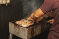 Hand of young man grilling some meat and fish on long rectangular barbecue with smoke on the street outdoor. Royalty Free Stock Photo