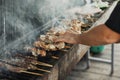 Hand of young man grilling some meat and vegetables on long rectangular barbecue with smoke on the street outdoor. Royalty Free Stock Photo