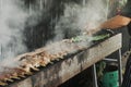 Hand of young man grilling some meat and vegetables on long rectangular barbecue with smoke on the street outdoor. Royalty Free Stock Photo