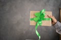 Hand of a young man holding a gift box with green ribbon on a gray background. Present for St.Patricks day Royalty Free Stock Photo