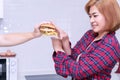 Hand of man holding hamburger for his girlfriend in the kitchen. Young woman refusing say no getting junk food for her Royalty Free Stock Photo