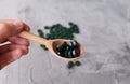 Hand of young man holding wooden spoon with chlorella tablets. Chlorella is a single-celled green algae, it is used to make nutrit