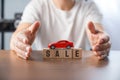 Hand of young man protecting toy car on wooden cube with SALE text on table Royalty Free Stock Photo