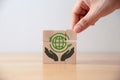 Hand of young man put wooden cube with green world icon.