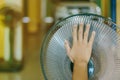 Hand of Young man touch and adjust on front grills of electric fan for a good wind in his home in summer