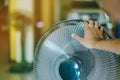 Hand of Young man touch and adjust on front grills of electric fan for a good wind in his home in summer of april