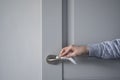 The hand of a young woman cleans and disinfects the doorknob of an open gray door during the period of isolation and as prevention