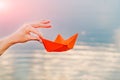 Hand of a young woman holding a paper boat by her fingers above the river in the summer Royalty Free Stock Photo