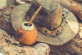 Handcrafted Artisan Yerba Mate Tea Calabash Gourd with Straw Leather Hat on Wood Logs in Forest. Travel Wanderlust Concept