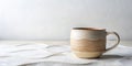A handcrafted ceramic mug with a beige and tan wavy design sits on a textured off-white surface against a neutral backdrop. Royalty Free Stock Photo