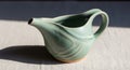 Handcrafted ceramic pitcher with crackled celadon glaze and curved handle casting shadow on white textured surface in natural Royalty Free Stock Photo