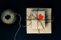 Handcrafted gift box wrapped in Craft paper with red wooden heart, rope and bow on black background. Top view, flat lay, toned Royalty Free Stock Photo