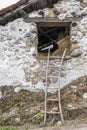 A handcrafted ladder leaning against the facade of a rural farmhouse giving access to a barn or granary full of bales of straw