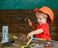 Handcrafting concept. Toddler on busy face plays with hammer tool at home in workshop. Child in helmet cute playing as