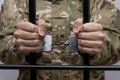 A handcuffed soldier clutches the bars with his hands against a light background. Concept: trial of a soldier in the army, diserte