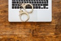 Handcuffs on a laptop, wooden office desk background, top view Royalty Free Stock Photo