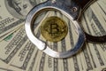 Handcuffs on hundred dollar bills and a gold bitcoin coin. Close-up