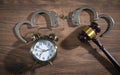 Handcuffs, judge gavel and alarm clock on the wooden background