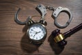 Handcuffs, judge gavel and alarm clock on the wooden background