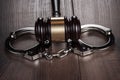 Handcuffs and judge gavel on brown wooden table