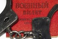 The handcuffs lie on the Russian military ticket, a selective focus. Concepts: universal mobilization, coercion and intimidation,