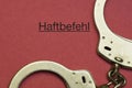 handcuffs next to the german word haftbefehl, translation arrest warrant on a red paper background