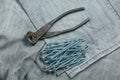 A handful of metallic self-cutters screws and very aged and rusty pliers lies on backdrop of an old denim fabric