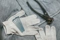 A handful of metallic self-cutters screws and very aged and rusty pliers lies on Safety knitted Work Gloves for