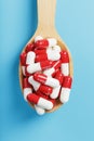 A handful of Red and white pill capsules in a wooden spoon on a blue background Royalty Free Stock Photo