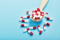 A handful of Red and white pill capsules in a wooden spoon on a blue background Royalty Free Stock Photo