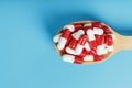 A handful of Red and white pill capsules in a wooden spoon on a blue background Royalty Free Stock Photo