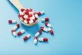 A handful of Red and white pill capsules in a wooden spoon on a blue background Royalty Free Stock Photo
