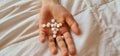 Handful of white round pills in child palm on bed. Hand holds bunch of small round medicines