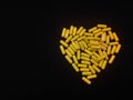 A handful of yellow pills in the shape of a heart on a black background. View from above. Copy space. Royalty Free Stock Photo