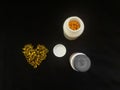 A handful of yellow pills in the shape of a heart and two jars on a black background. View from above. Copy space. Royalty Free Stock Photo