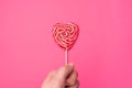 Handholds red heart-shaped lollipop candy isolated on an empty colorful pink background. Symbol of love for Happy Women