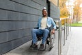 Handicapped accessible city. Positive impaired Afro man in wheelchair leaving building on ramp outdoors in autumn Royalty Free Stock Photo
