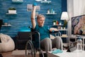 Handicapped senior woman holding trainer dumbbells doing arms exercise